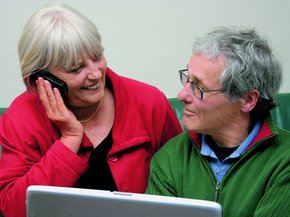 Stariji par ispred laptop računara, međusobno se gledaju dok žena priča telefonom